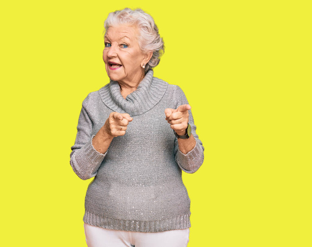 Старшая седовласая женщина в обычном зимнем свитере указывает пальцем в камеру со счастливым и смешным лицом. хорошая энергия и вибрации.  - Фото, изображение