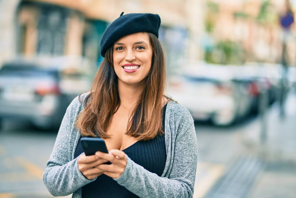 Young latin woman wearing french style using smartphone at the city. - Photo, Image