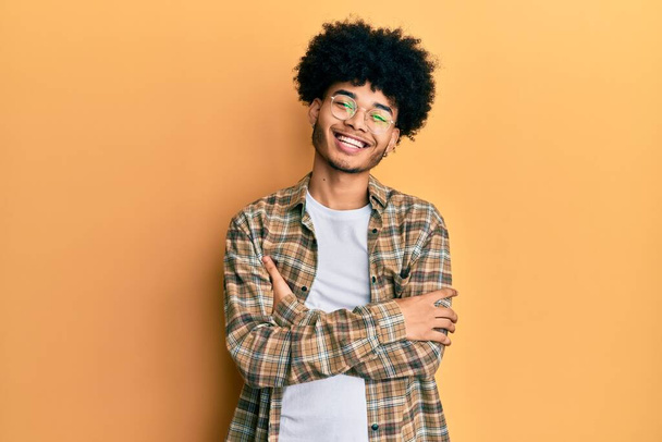 Mladý africký Američan s afro vlasy na sobě ležérní oblečení šťastný obličej s úsměvem se zkříženýma rukama dívá do kamery. pozitivní osoba.  - Fotografie, Obrázek