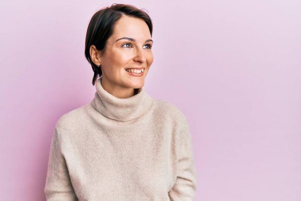 Young brunette woman with short hair wearing casual winter sweater looking away to side with smile on face, natural expression. laughing confident.  - Fotoğraf, Görsel