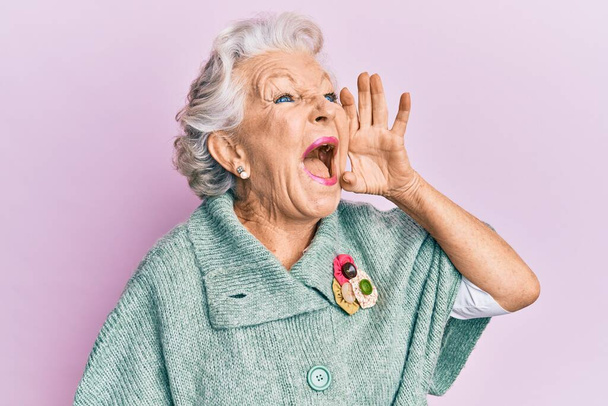 Mujer mayor de cabello gris con ropa casual gritando y gritando fuerte a un lado con la mano en la boca. concepto de comunicación.  - Foto, Imagen