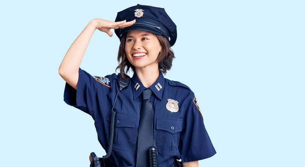 Joven chica hermosa vistiendo uniforme de policía muy feliz y sonriente mirando lejos con la mano sobre la cabeza. concepto de búsqueda.  - Foto, Imagen
