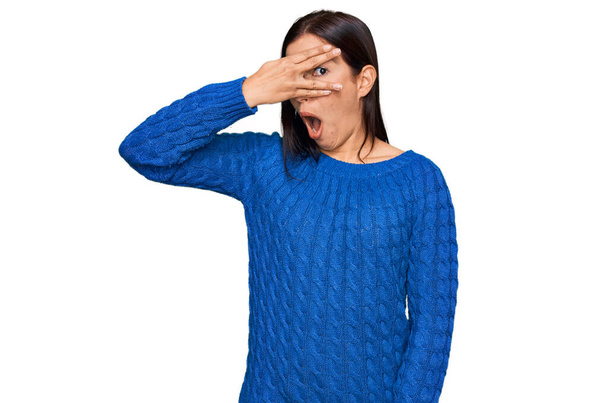 Jonge Spaanse vrouw draagt casual kleding gluren in shock bedekken gezicht en ogen met de hand, kijken door vingers met beschaamde uitdrukking.  - Foto, afbeelding