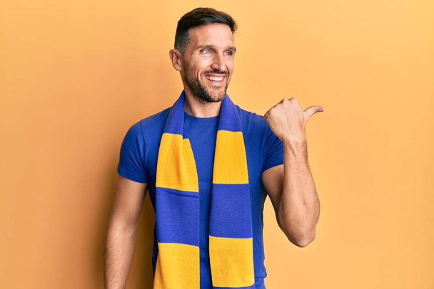 Schöner Mann mit Bart Fußball Hooligan Jubelspiel zeigt Daumen nach oben zur Seite lächelt glücklich mit offenem Mund  - Foto, Bild