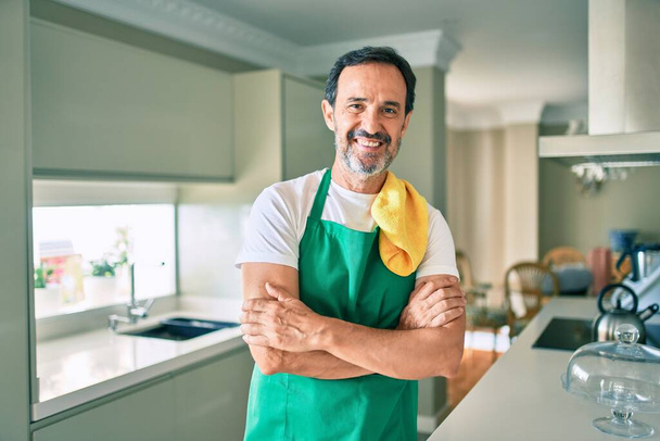 Uomo delle pulizie di mezza età con la barba sorridente felice in piedi in cucina - Foto, immagini