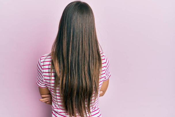 Молода брюнетка в повсякденному одязі над рожевим тлом, стоячи позаду, дивлячись з схрещеними руками
  - Фото, зображення