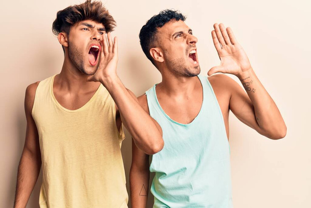 Giovane coppia gay indossa vestiti casual urlando e urlando forte a lato con mano sulla bocca. concetto di comunicazione.  - Foto, immagini