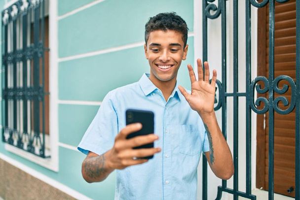 Jovem latino sorrindo feliz fazendo videochamada usando smartphone na cidade. - Foto, Imagem