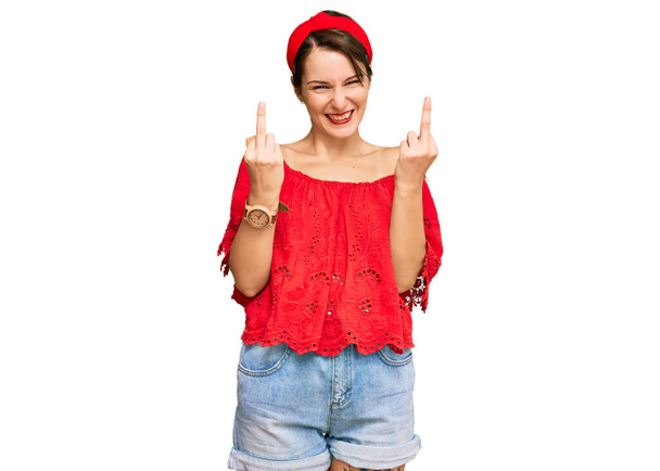 Young brunette woman with short hair wearing casual summer clothes and diadem showing middle finger doing fuck you bad expression, provocation and rude attitude. screaming excited  - Foto, imagen