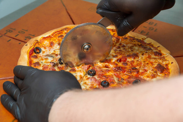 Cutting pizza with a round cutter knife. Close-up of delicious pizza being cut into pieces. - Photo, Image