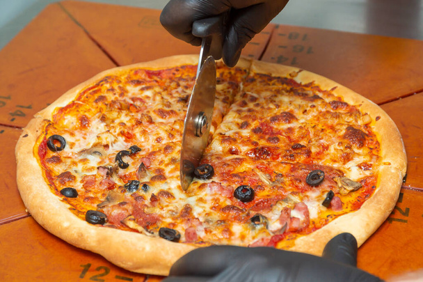 丸型のカッターナイフでピザを切る。おいしいピザが切られる終わり. - 写真・画像