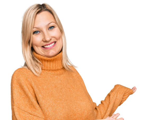 Middle age caucasian woman wearing casual winter sweater inviting to enter smiling natural with open hand  - Fotografie, Obrázek