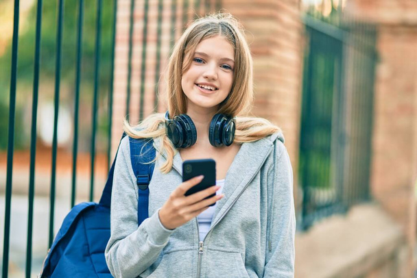 Beautiful caucasian student teenager smiling happy using smartphone at the city. - Photo, image
