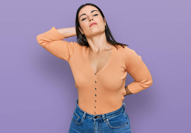 Junge hispanische Frau in lässiger Kleidung, die unter Nackenschmerzen, Berührung des Nackens mit der Hand und Muskelschmerzen leidet  - Foto, Bild