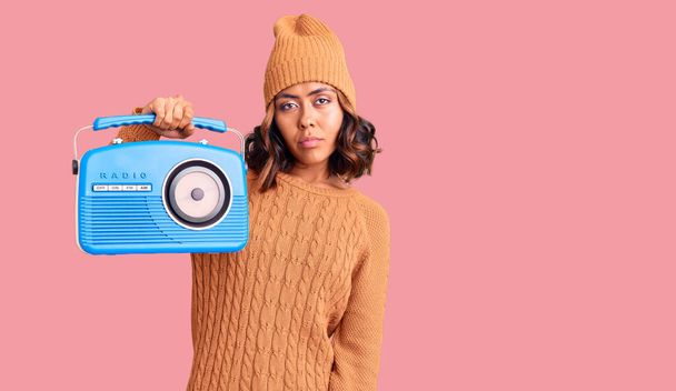Mladý krásný smíšený závod žena drží vintage radio myšlení postoj a střízlivý výraz hledá sebevědomí  - Fotografie, Obrázek