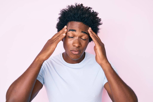 Knappe Afro-Amerikaanse man met afrohaar in casual kleding die lijdt aan hoofdpijn wanhopig en gestrest omdat pijn en migraine. handen op het hoofd.  - Foto, afbeelding