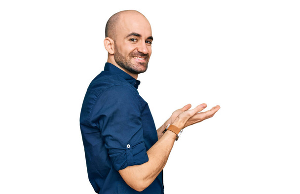 Junger hispanischer Mann in lässiger Kleidung, die zur Seite zeigt, mit den Händen geöffnete Handflächen, die Kopierraum zeigen, Werbung lächelnd aufgeregt glücklich  - Foto, Bild