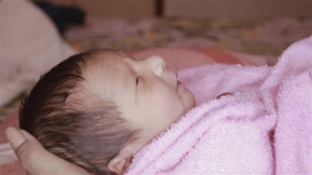 Όμορφο νεογέννητο μωρό αγόρι closeup (6 ημερών) που βρίσκεται στην αγκαλιά της μητέρας στο προγεννητικό νοσοκομείο. Παιδί τυλιγμένο σε κουβερτούλα (ζεστά ρούχα) χαμογελώντας και κοιτάζοντας. Η μητέρα του παρηγορεί και ξεκουράζει το μωρό της.. - Πλάνα, βίντεο
