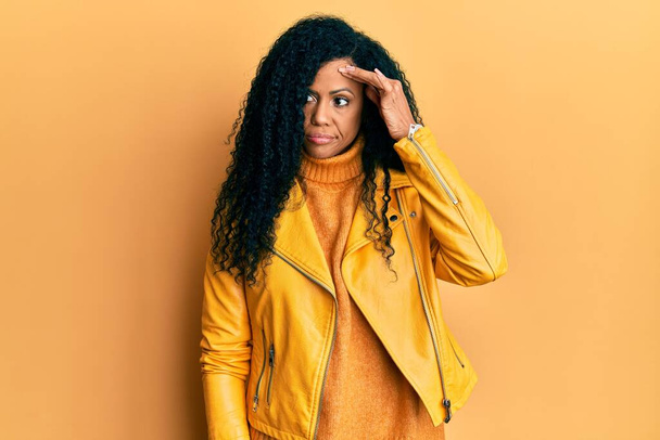 Mulher afro-americana de meia idade vestindo camisola de inverno de lã e jaqueta de couro preocupado e estressado sobre um problema com a mão na testa, nervoso e ansioso para a crise  - Foto, Imagem