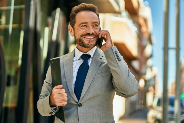 Middle age businessman smiling happy talking on the smartphone at the city. - 写真・画像