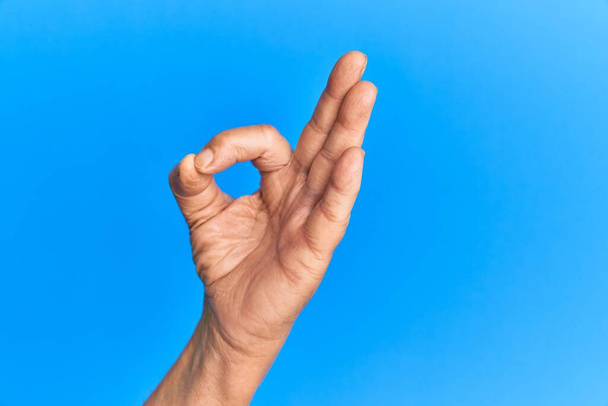 Hand eines hochrangigen hispanischen Mannes über blauem isoliertem Hintergrund gestikuliert zustimmend und macht Okay-Symbol mit den Fingern  - Foto, Bild