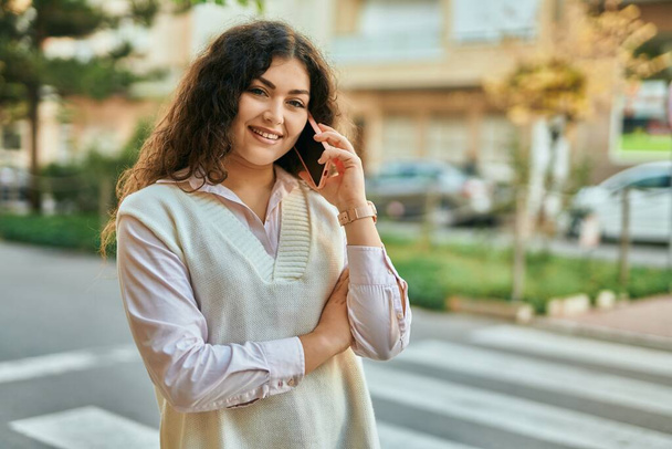 Genç İspanyol kadın gülümsüyor. Şehirdeki akıllı telefondan konuşuyor.. - Fotoğraf, Görsel