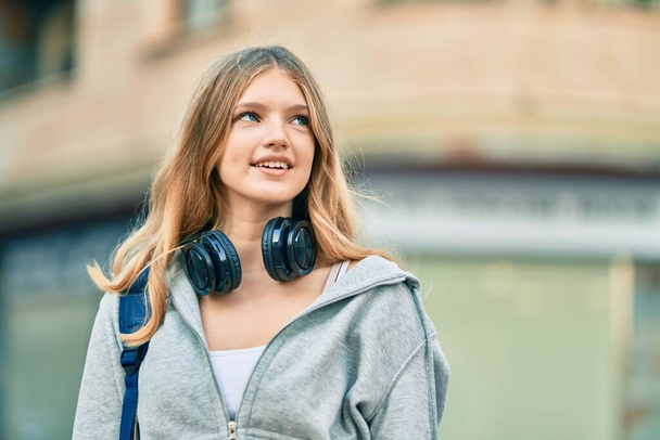 Kaunis valkoihoinen opiskelija teini hymyilevä onnellinen käyttäen kuulokkeet kaupungin. - Valokuva, kuva