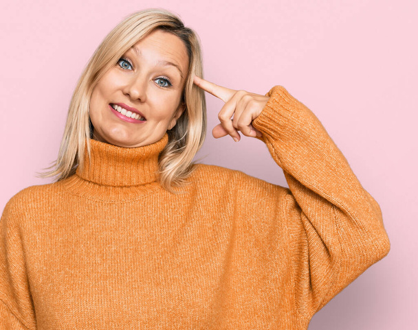 Mujer caucásica de mediana edad con suéter de invierno casual sonriendo apuntando a la cabeza con un dedo, gran idea o pensamiento, buena memoria  - Foto, Imagen