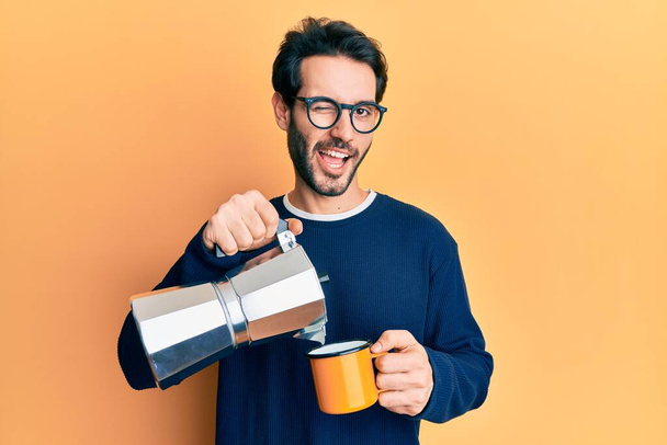 Молодий гізпанічний чоловік п'є каву італійського типу, що підморгує, дивлячись на камеру з сексуальним виразом, веселим і щасливим обличчям..  - Фото, зображення