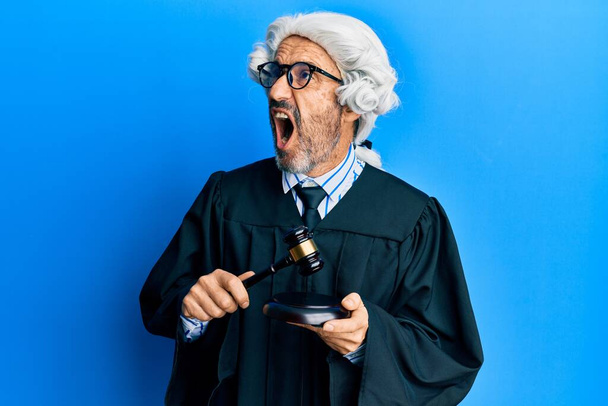 Middle age hispanic man using gavel angry and mad screaming frustrated and furious, shouting with anger. rage and aggressive concept.  - Photo, Image