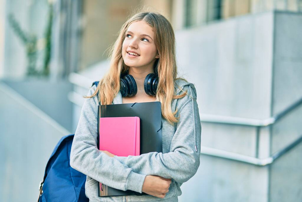Estudante caucasiano bonito adolescente sorrindo feliz usando fones de ouvido na cidade. - Foto, Imagem