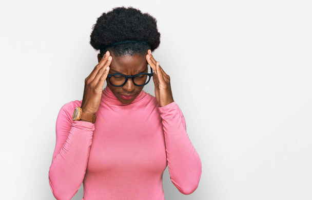Giovane ragazza afroamericana indossa abiti casual e occhiali con la mano sulla testa per il dolore alla testa perché lo stress. emicrania.  - Foto, immagini