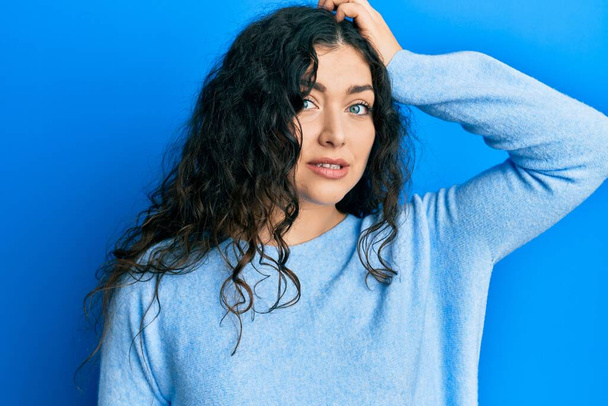 Young brunette woman with curly hair wearing casual clothes confuse and wonder about question. uncertain with doubt, thinking with hand on head. pensive concept.  - Photo, Image