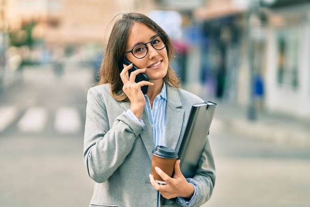 Młoda latynoska bizneswoman rozmawiająca przez smartfona i pijąca zabiera kawę do miasta. - Zdjęcie, obraz