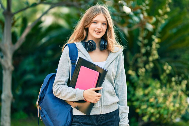 Kaunis valkoihoinen opiskelija teini hymyilee onnellinen käyttäen kuulokkeet puistossa. - Valokuva, kuva
