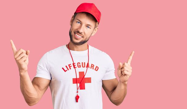 ライフガードのTシャツを着た若い白人男性は、さまざまな方向に指で自信を持って指して笑顔笛を吹いています。広告のコピースペース  - 写真・画像