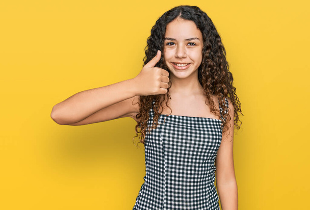 Teenager hispanic girl wearing casual clothes doing happy thumbs up gesture with hand. approving expression looking at the camera showing success.  - Photo, Image