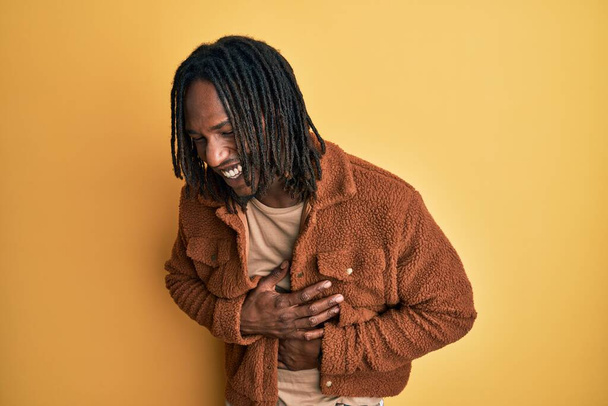 African american man with braids wearing brown retro jacket smiling and laughing hard out loud because funny crazy joke with hands on body.  - Zdjęcie, obraz