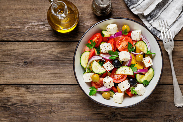 Klasyczna grecka sałatka ze świeżymi warzywami, serem feta i oliwkami. Zdrowe jedzenie. Drewniane tło. Widok z góry - Zdjęcie, obraz