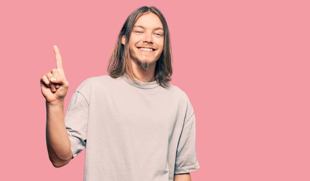 Handsome caucasian man with long hair wearing casual clothes showing and pointing up with finger number one while smiling confident and happy.  - Фото, зображення