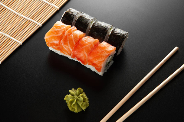 sushi na černém pozadí. Sushi California vedle bambusových tyčinek a wasabi - Fotografie, Obrázek