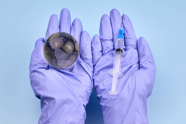Vrouwenhanden in medische handschoenen houden een aardbol en een spuit vast, het concept van vaccinatie.. - Foto, afbeelding