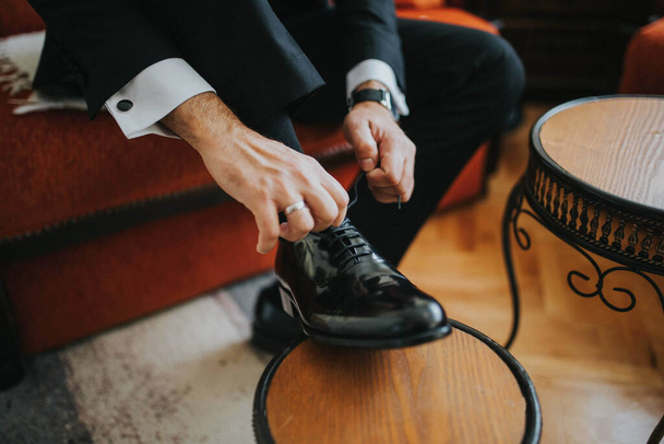 An elegant groom in a black suit tying his shoe on a wedding day - Photo, Image