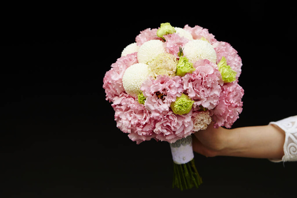 A closeup of a woman's hand holding a peonies flower bouquet, in front of a black background - Fotografie, Obrázek