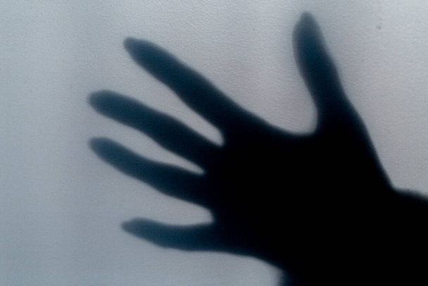 ein verschwommener Schatten einer Hand auf einer bemalten Wand, der Schatten der Hand einer Frau in Großaufnahme - Foto, Bild