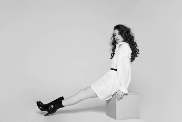 Ganzkörperansicht einer Brünetten mit langen Haaren, junge Frau in weißem Hemd und High Heel, die im Studio posiert. Schwarz-Weiß-Bild. - Foto, Bild