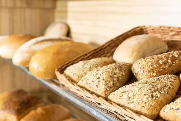 A freshly baked triangular-shaped bun with various seeds is on the shelf of a bakery store. - Foto, Imagen