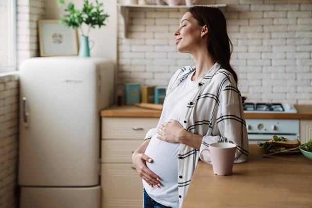 Pregnant happy nice woman smiling while having breakfast in home kitchen - Foto, immagini