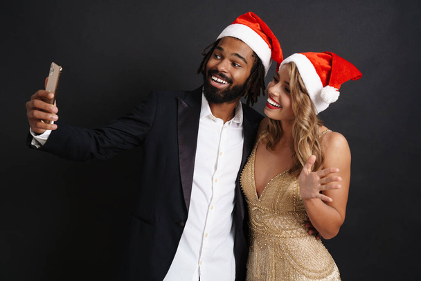 Couple in smart wear celebrating holiday party taking a selfie isolated on black background - Zdjęcie, obraz