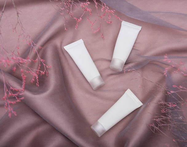 Tubos blancos de crema sobre un fondo de seda marrón claro y rama decorativa - Foto, imagen